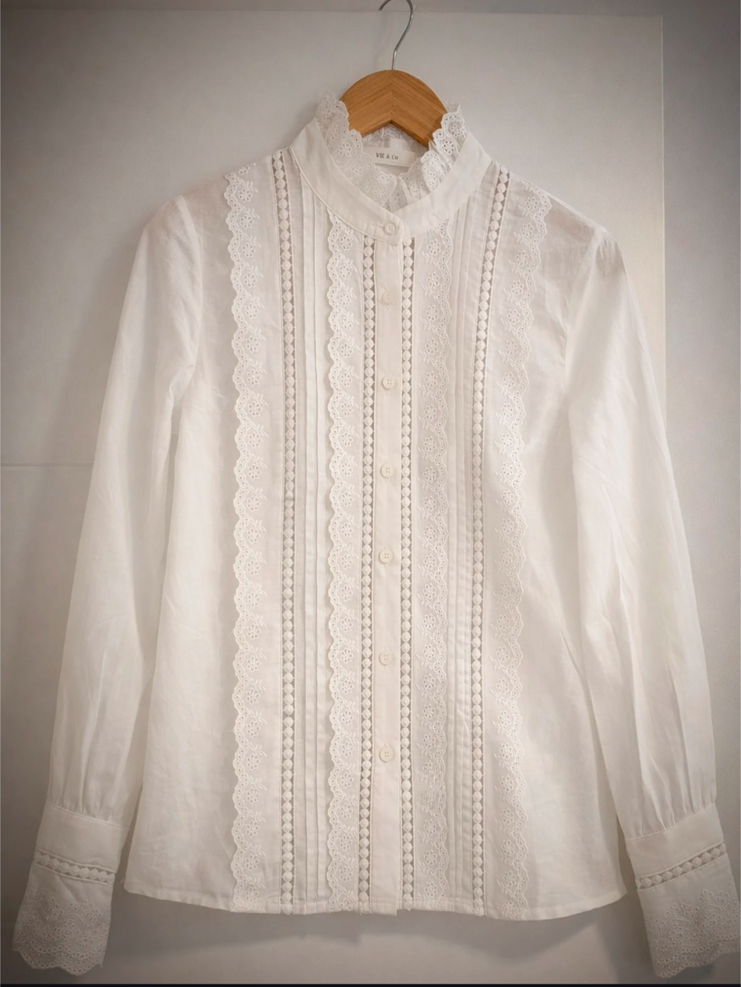 Blusa blanca con encaje y bordado en percha mostrando detalle frontal completo
