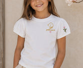 Niña sonriendo con la camiseta Fleur puesta, junto a una rama de flores rosas