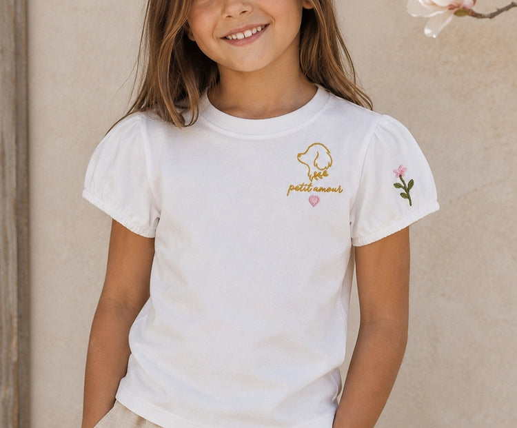 Niña sonriendo con la camiseta Fleur puesta, junto a una rama de flores rosas